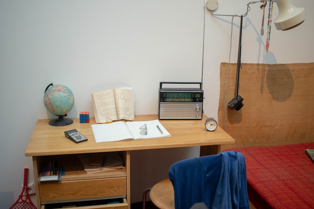 Studentenkamer met bureau, boeken en een bed bij het raam