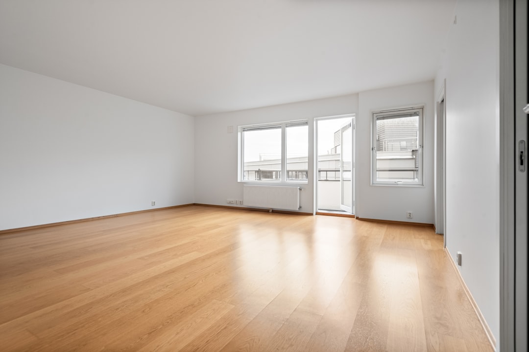 Lege kamer met houten vloer, groot raam en radiator tijdens een bezichtiging